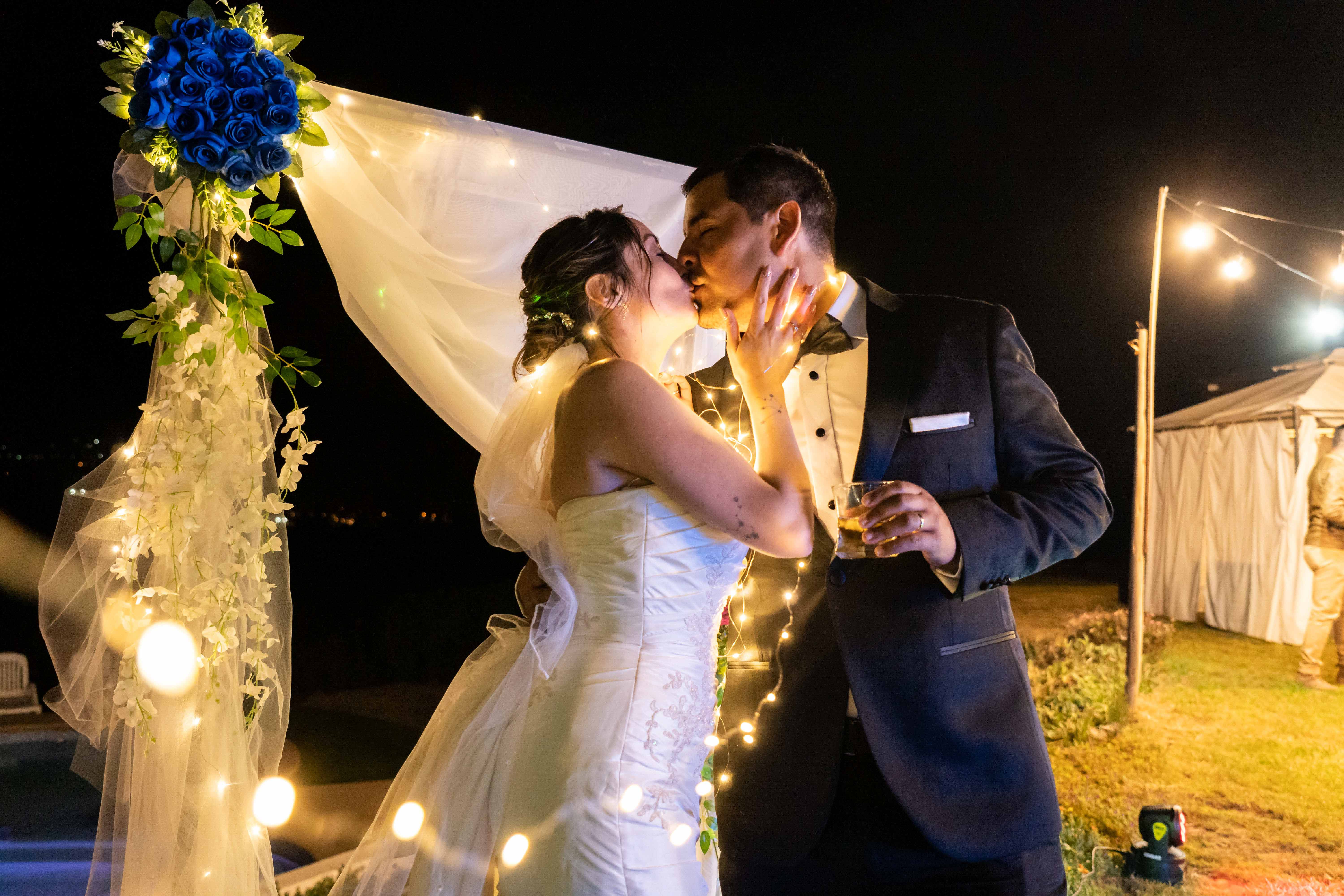 Los recién casados se abrazan sobre un altar hermosamente iluminado, sellando su amor con un beso.