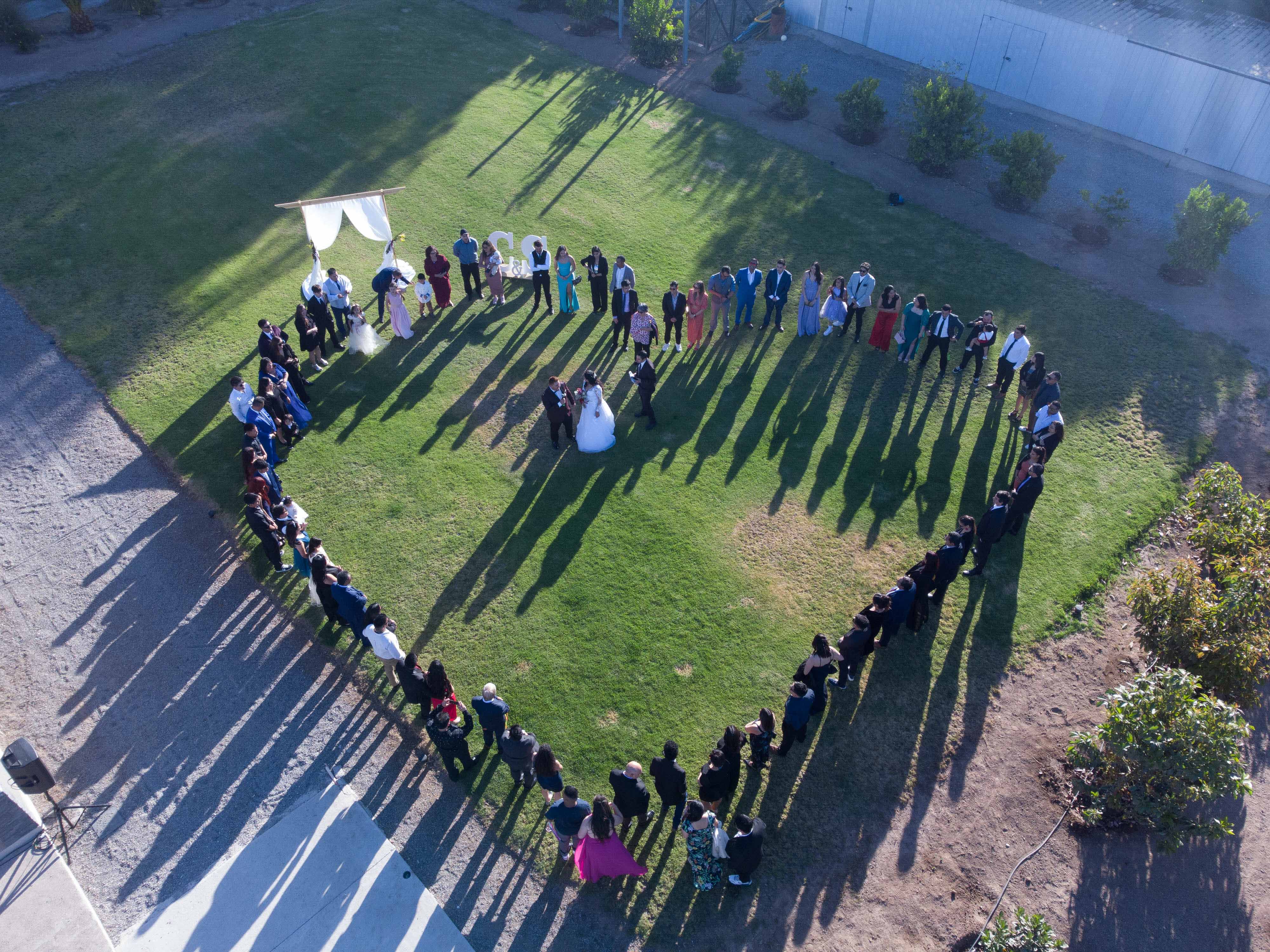 Pareja de recién casados bailando en el centro de un corazón formado por los asistentes a su matrimonio. Fotografía de dron.