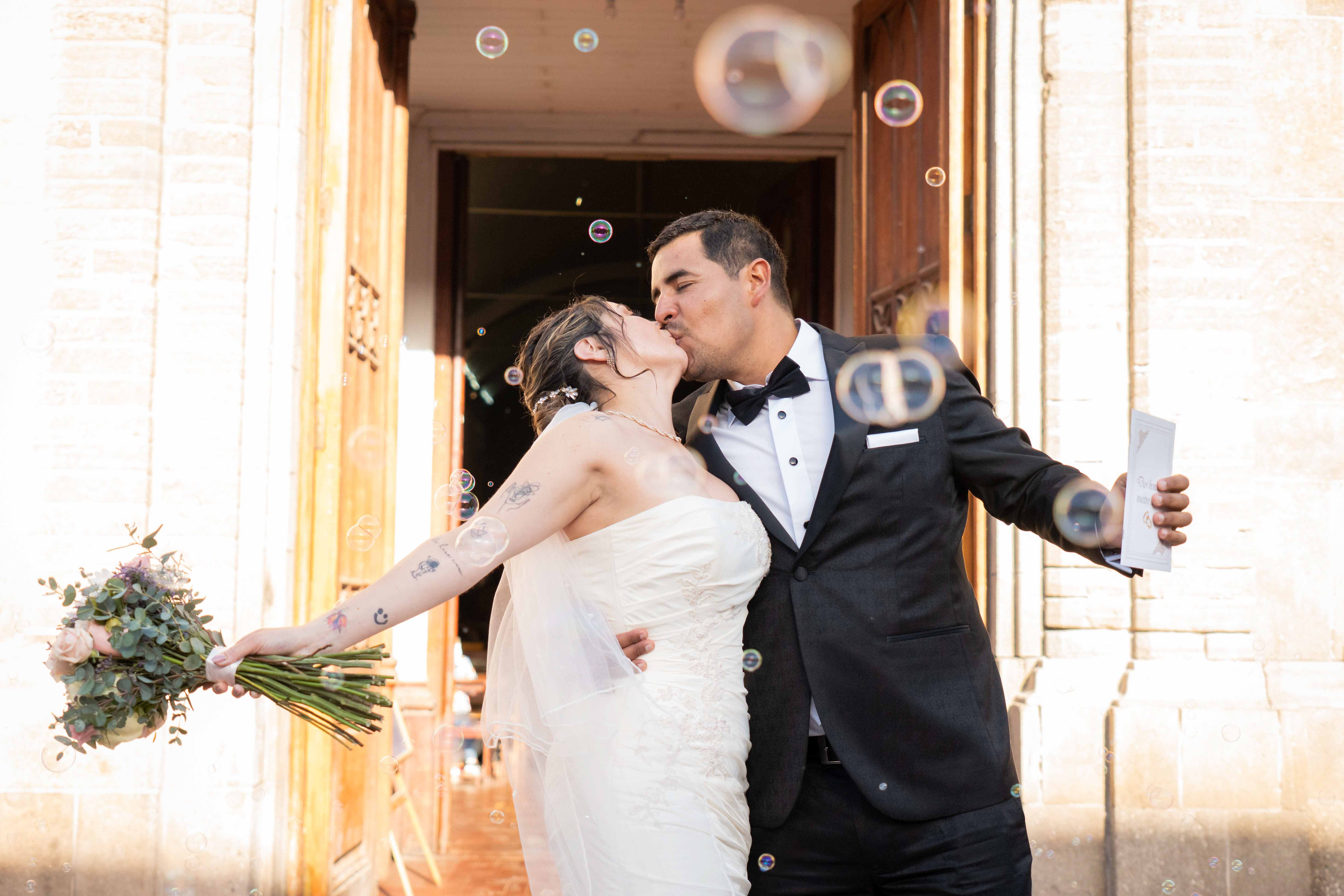 Una pareja de recién casados comparte un tierno beso fuera de la iglesia rodeados de burbujas flotantes el día de su boda.